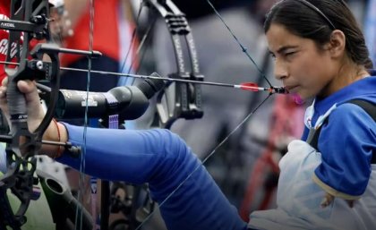 a woman sits in a chair and draws a bow with her foot and mouth